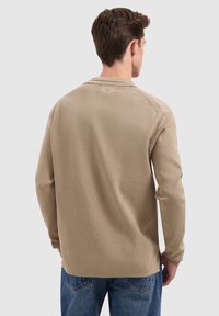 Beige longsleeve shirt met ronde hals en textuurstof, met raglanmouwen en een losse pasvorm. Gecombineerd met blauwe spijkerbroeken.