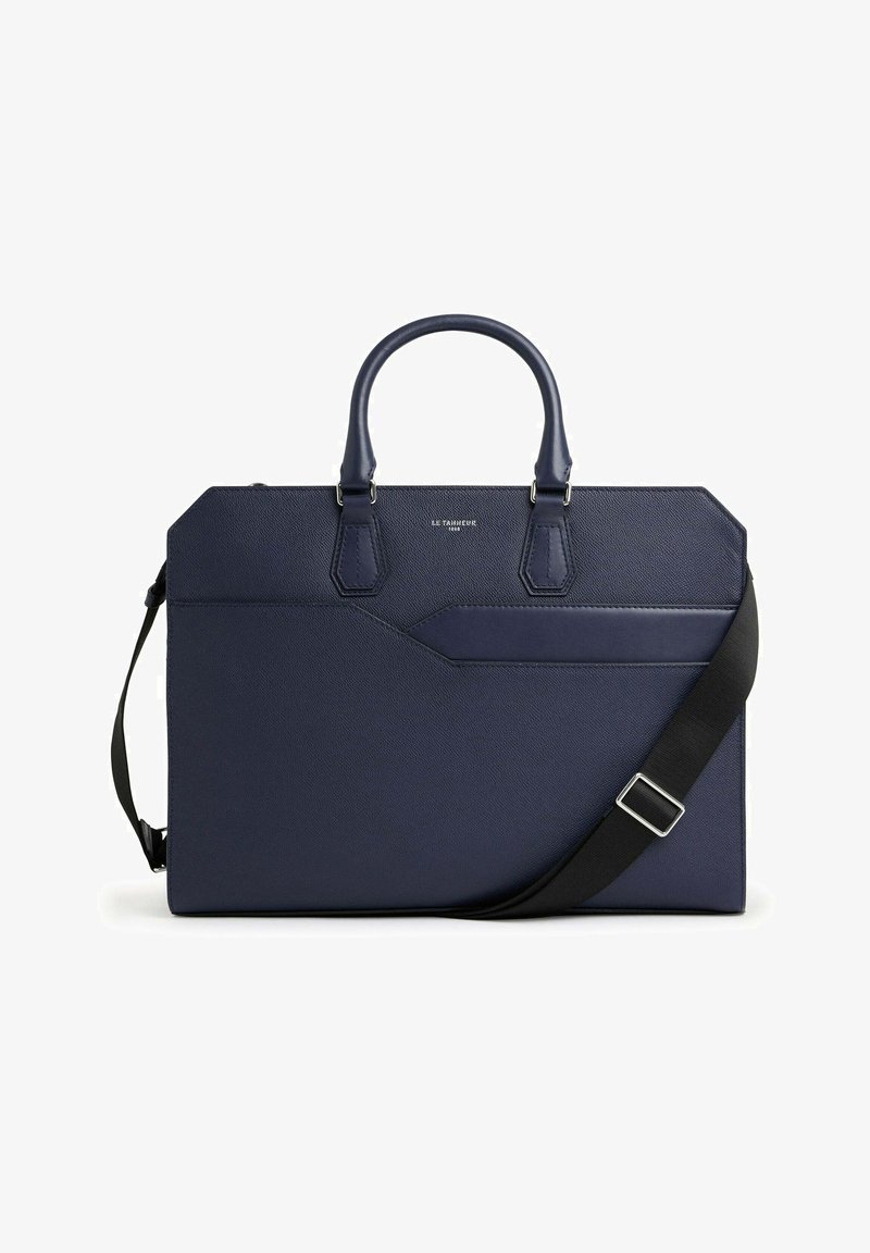 Bolso de cuero texturizado en color navy con asas dobles y una correa negra desmontable. Presenta un bolsillo frontal y elementos de diseño geométrico.