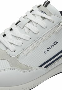 Sneaker bianca con tomaia in pelle liscia e dettagli testurizzati, design con lacci, particolare logo e striscia blu lungo la suola.