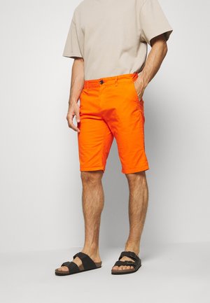 Oranžové bavlněné šortky s knoflíkovým zapínáním, bočními kapsami a volným střihem. Kombinováno s černými sandály s nastavitelnými pásky.