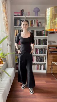 Must have lühikeste varrukatega must peamine topp ja ruudukujuline kaelus, sobitatud laia musta pükstega. Riietust täiendab paar spordijalatsit ja nähtavad tätoveeringud.