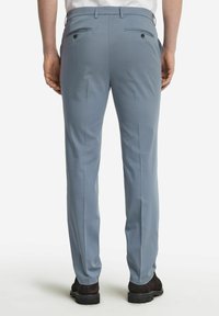 Ljusblå byxor gjorda av slät tyg, med två bakfickor med knappar och pressveck ned längs benen. Bärs med svarta skor.