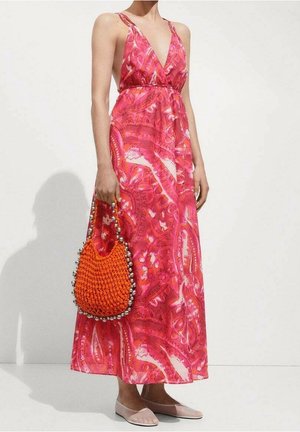 Pink, patterned maxi dress with a deep V-neck, thin straps, and a cinched waist; paired with an orange woven bag and beige flats.