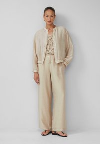 Bomber jacket beige leggero, top in crochet e pantaloni a gamba larga. Tessuto morbido con polsini elastici. Infradito nere completano l'outfit.