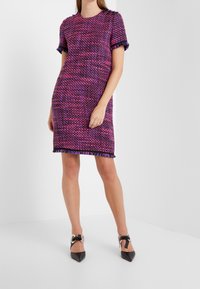 Kratký rukáv, šatník po kolena z fialové a růžové tkaniny s třásněmi na spodním lemu a dekorativními knoflíky na ramenou.