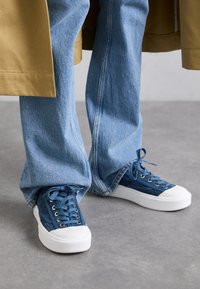 Denimsneakers i mørkeblå med hvite gummisåler. Har klassisk snøring, teksturert stoff og kontrasterende tåhette.