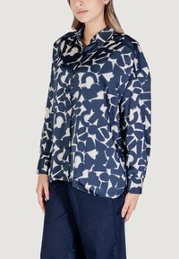 Camicia blu navy con bottoni, decorata con motivi astratti bianchi, maniche lunghe e colletto; realizzata in tessuto liscio con una vestibilità comoda.