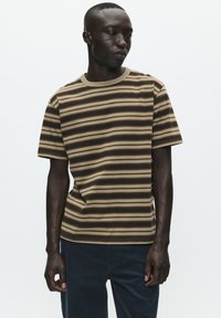 Stripet t-shirt lavet af blødt stof med vandrette brune, beige og creme striber. Har en ribbet halsudskæring og korte ærmer.