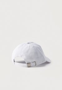 Casquette de baseball en coton blanc posée sur une surface blanche, montrant la sangle réglable et la boucle métallique à l'arrière.