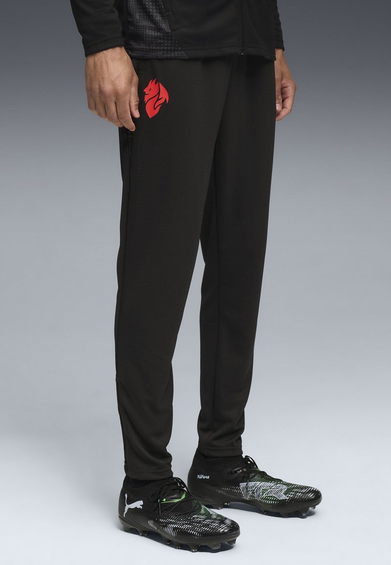 Pantaloni sportive neri con logo rosso, realizzati in tessuto liscio, con un design tapered, abbinati a scarpini da calcio neri e verdi.