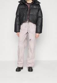 Czarna krótka kurtka puchowa z puchowymi rękawami, czarno-szara koszula w paski, jasnoróżowe luźne jeansy z przetarciami oraz czarne buty.