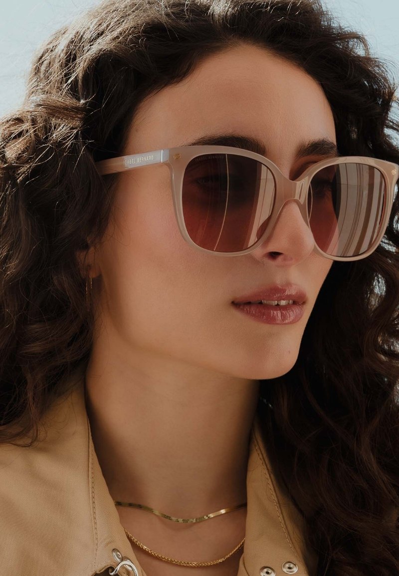 Beige übergroße Sonnenbrille mit verlaufenden braunen Gläsern, die transparente Fassung und subtile metallische Details am Bügel aufweist.