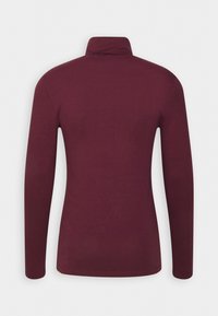Camisa ajustada de manga larga en tejido burdeos oscuro con cuello alzado y textura suave, sin patrones ni cierres visibles.