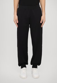 Svarta joggingbyxor i mjukt material, med en avslappnad passform och elastisk midja. Kombineras med vita sneakers för kontrast.