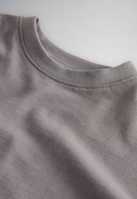 Primo piano di un tessuto morbido grigio con scollo rotondo che mostra cuciture dettagliate e una texture liscia su uno sfondo chiaro.