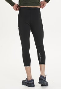 Svarta sportleggings med en åtsittande design, utrustade med sidofickor och reflexdetaljer. Materialet verkar ha en texturerad och elastisk kvalitet.