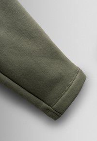 Olivnozeleni tekstilni rokav z gladko strukturo, ki ima ravno manšeto in urejen šiv ob robu.