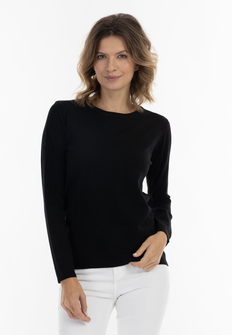 Pulover negru cu mânecă lungă și guler rotund, realizat dintr-un material moale. Purtați cu pantaloni albi, are o formă ajustată și manșete cu dungi.