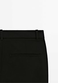 Pantalon noir au design épuré, avec une texture lisse, une ceinture et une poche arrière unique sans éléments métalliques visibles.