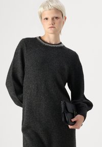 Robe pull gris foncé avec un col rond orné d'embellissements en argent. Manches longues et volumineuses, avec une texture lisse. Tient une pochette en cuir noir.