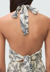 Trägerloses, cremefarbenes Haltertop mit marineblauem Blattmuster; verfügt über einen offenen Rücken mit gebundenen Trägern, hervorgehoben durch die glatte Stofftextur.