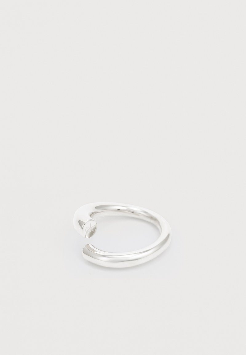Anillo abierto de plata con un diseño suave y redondeado. Presenta un logo sutil en un extremo y un acabado pulido, que exhibe un aspecto elegante y moderno.