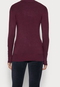 Bordowy sweter z dzianiny z długim rękawem, okrągłym dekoltem i dopasowanymi mankietami, o gładkiej fakturze i lekko wydłużonym tylnym obszyciu.