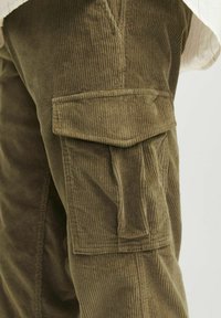 Olive green corduroy cargo pants with vertical ribbed texture, featuring a side pocket and a relaxed fit design.