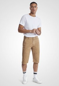 Lys brune kne-lange shorts laget av bomull, med beltehemper og sidelommer, kombinert med en enkel hvit t-skjorte med rund hals og hvite joggesko.