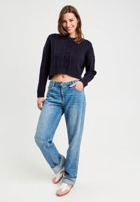 Granatowy sweter z wyszywanym wzorem, luźne jasnoniebieskie dżinsy i białe sneakersy z różowymi akcentami. Swobodny krój z podwiniętymi spodniami.