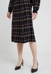 Vestido negro hasta la rodilla con patrón cuadriculado en rosa y dorado, puños acanalados, combinado con tacones slingback negros de punta puntiaguda. Tela texturizada.