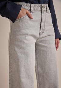 Grijze high-waisted jeans in een relaxte pasvorm met een rechte pijp. Voorzien van een knoopsluiting, voorzakken en subtiele vervaging in de stof.