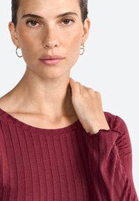 Top mauve côtelé avec un col rond et des manchettes légèrement froncées, présentant des manches longues et une texture lisse.