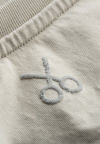 Lichtbeige stof met een textuur en een lichtgrijze geborduurde schaarontwerp. Het materiaal lijkt zacht met een geribbelde tailleband.