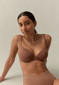 Pruun õmblusteta rinnahoidja reguleeritavate rihmade, vormitud tassidega ja peente õmblustedetailidega, mis on kombineeritud sobivate, kõrge vöökohaga aluspükstega samas toonis.