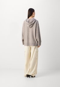 Sudadera de punto beige de gran tamaño con una textura sutil, que presenta una costura en la parte trasera y un corte relajado, combinada con pantalones cargo beige amplios.