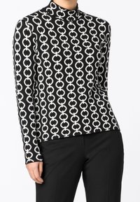 Maglia a maniche lunghe con collo alto, caratterizzata da un motivo circolare in bianco e nero su un tessuto a maglia. Il design è aderente e elegante.