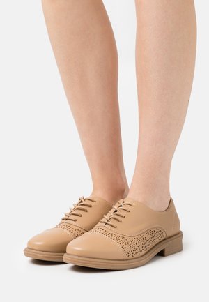 Oxfords en cuir beige avec fermeture à lacets, détails perforés sur la boîte à orteils, forme de pointure arrondie et talon plat de style bois.