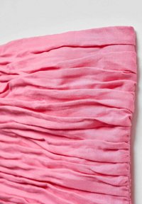 Un tissu rose froncé avec une surface texturée, présentant des plis régulièrement espacés, mettant en valeur un matériau doux et léger.