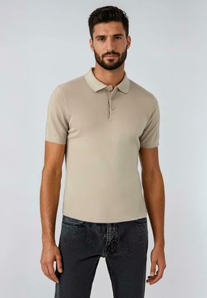 Beige poloshirt met korte mouwen en een kraag, voorzien van drie knopen en een gladde textuur, gecombineerd met zwarte jeans met structuur.