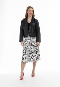 Czarna skórzana kurtka typu cropped z dwoma guzikami, połączona z spódnicą w zebra w czarno-białym wzorze sięgającą do kolan oraz czerwonymi szpilkami.