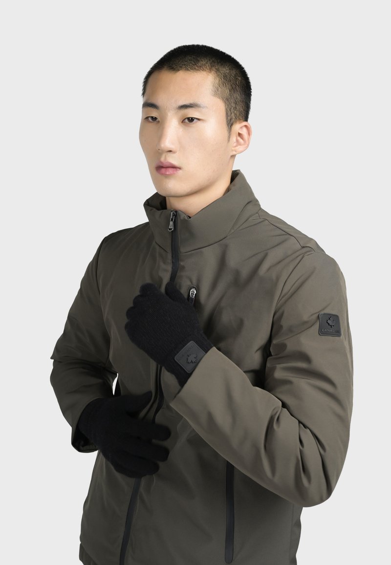 Olivgrön, vattentät jacka med hög krage och dragkedjestängning, kombinerad med svarta stickade handskar som har en logotyp-patch.