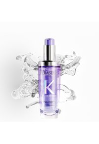 Flacon d'huile pour cheveux Purple Kerastase Blond Absolu avec pompe argentée sur fond de splash d'eau blanche.