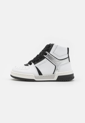 Białe sneakersy z wysoką cholewką z czarnymi akcentami i sznurowadłami. Posiadają srebrny metaliczny panel oraz perforowany wzór na nosku. Podeszwa z gumy zapewnia przyczepność.