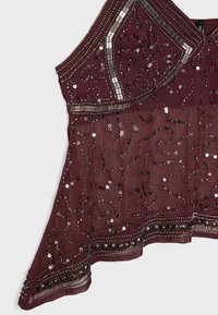 Top in tessuto borgogna con intricate decorazioni in perline nere e argento e paillettes in motivi ondulati, con orlo a onda e vestibilità morbida.