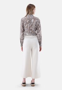 Top abbassato con motivo paisley in beige e marrone, abbinato a pantaloni larghi bianchi e mocassini neri. Texture del tessuto liscia.