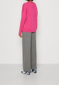 Suéter rosa oversize, pantalones de pierna ancha a rayas grises y tacones azules con estampado. Textura suave y corte relajado.