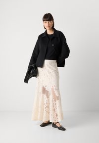 Black wool jacket, black top, cream lace skirt with floral pattern, layered texture, and black leather flats. Black handbag with woven detail.