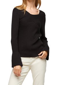 Svart ribbad tröja med fyrkantig halsringning, utsvängda långa ärmar och detaljer med texturerat mönster. Matchas med ljusa byxor.