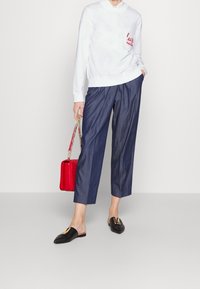 Vit sweatshirt med röd "love"-brodyr, blå avsmalnande byxor, svarta mules med gulddetaljer och en röd quiltad handväska.